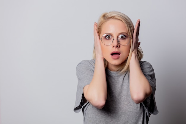 Mujer rubia seria en vidrios en la pared blanca