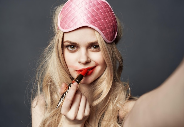 Mujer rubia sexy con emociones de lápiz labial rojo y máscara rosa en la cara
