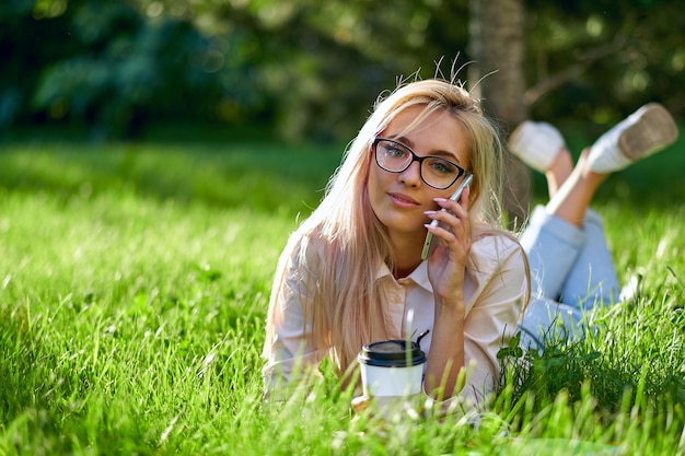 Mujer rubia sexy hablando por teléfono móvil y tumbada en la pradera