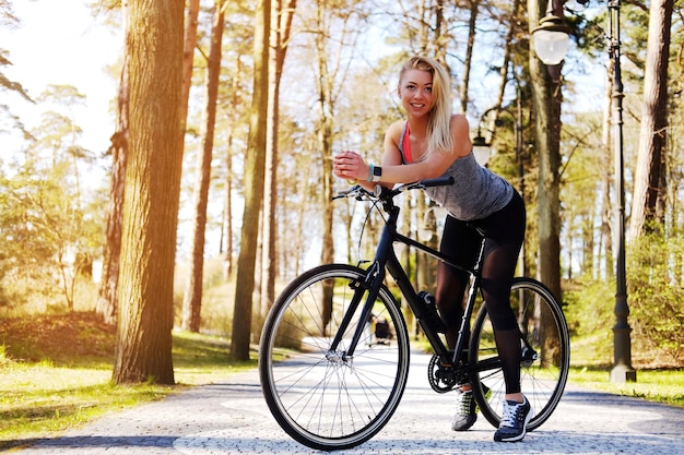 Mujer rubia sexy posando junto a la bicicleta en un parque de verano.