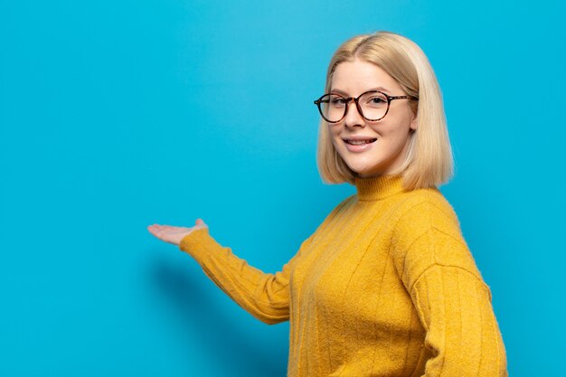 Mujer rubia sintiéndose feliz y alegre, sonriendo y dándote la bienvenida