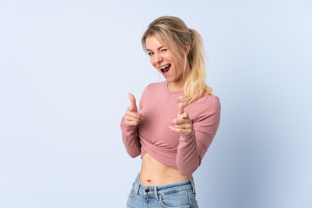 Mujer rubia sobre azul aislado apuntando hacia el frente y sonriendo