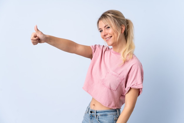 Mujer rubia sobre azul aislado dando un gesto de pulgares arriba