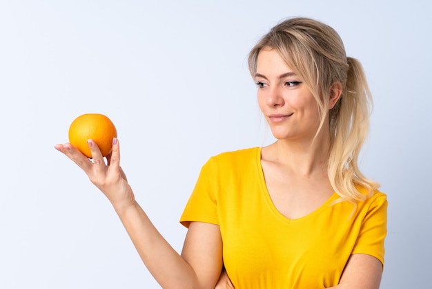 Mujer rubia sobre azul aislado sosteniendo una naranja