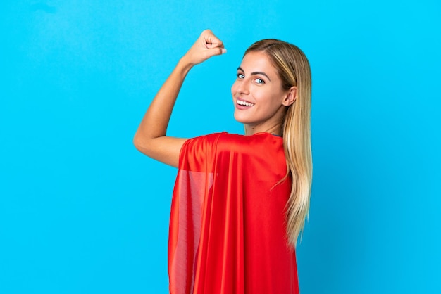 Mujer rubia sobre fondo aislado en traje de superhéroe y haciendo un gesto fuerte