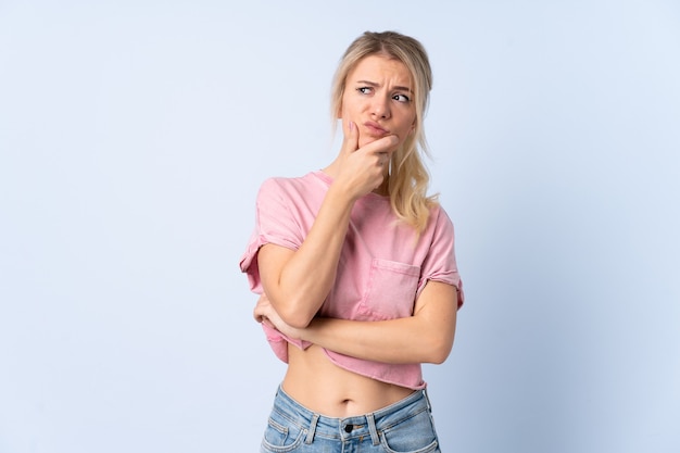 Mujer rubia sobre fondo azul aislado que tiene dudas