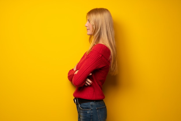 Mujer rubia sobre muro amarillo en posición lateral.