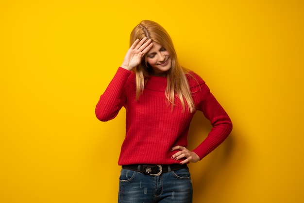 Mujer rubia sobre pared amarilla con expresión cansada y enferma