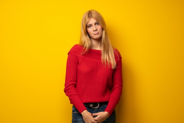 Mujer rubia sobre pared amarilla con expresión triste y deprimida