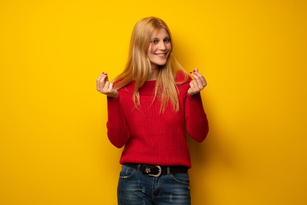 Mujer rubia sobre pared amarilla manteniendo una conversación con el teléfono móvil