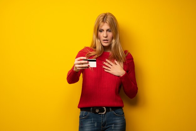 Mujer rubia sobre pared amarilla con teléfono inteligente roto con problemas