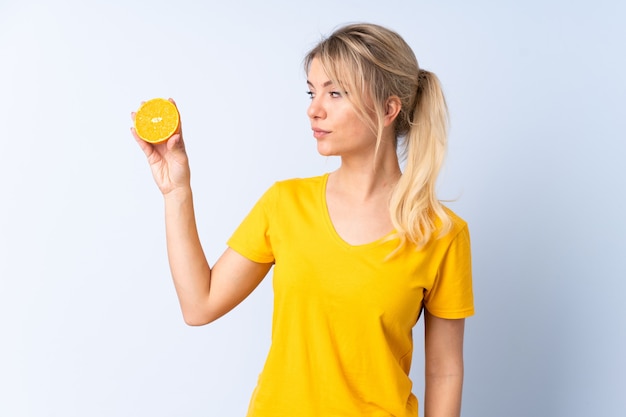 Mujer rubia sobre pared azul aislada sosteniendo una naranja