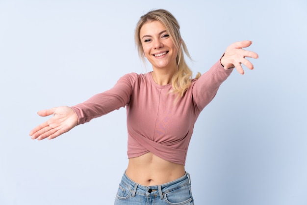 Mujer rubia sobre presentación azul aislada e invitando a venir con la mano