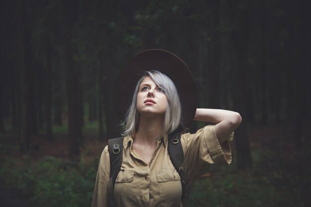 Mujer rubia con sombrero con mochila en día lluvioso en bosque