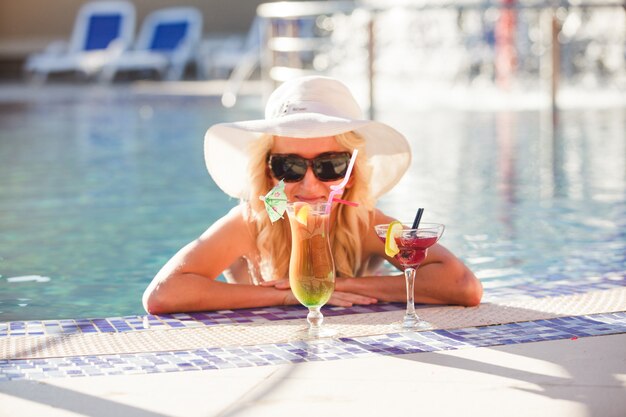 Mujer rubia con sombrero en la piscina