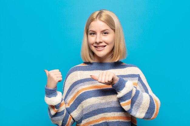 Mujer rubia sonriendo alegre y casualmente apuntando al espacio de la copia en el costado, sintiéndose feliz y satisfecha