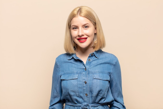 Mujer rubia sonriendo alegre y casualmente con una expresión positiva, feliz, segura y relajada