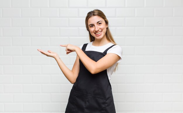 Mujer rubia sonriendo alegremente y apuntando al espacio de la copia en la palma lateral, mostrando o publicitando un objeto