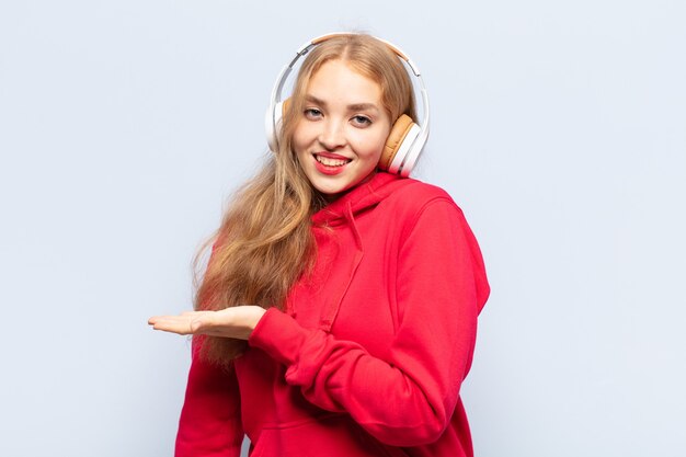 Mujer rubia sonriendo alegremente, sintiéndose feliz y mostrando un concepto en el espacio de la copia con la palma de la mano