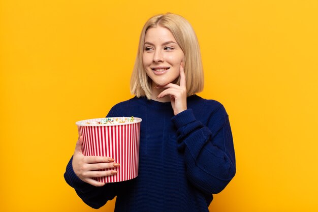 Mujer rubia sonriendo felizmente y soñando despierto o dudando, mirando hacia el lado