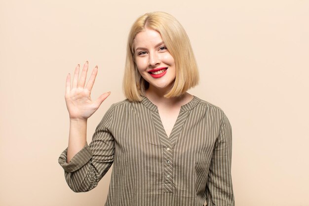 Mujer rubia sonriendo y mirando amistosamente, mostrando el número cinco o quinto con la mano hacia adelante, contando hacia atrás