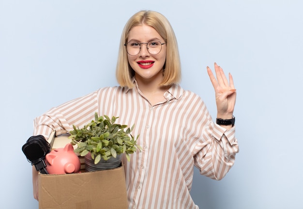 Mujer rubia sonriendo y mirando amistosamente, mostrando el número cuatro o cuarto con la mano hacia adelante, contando hacia atrás