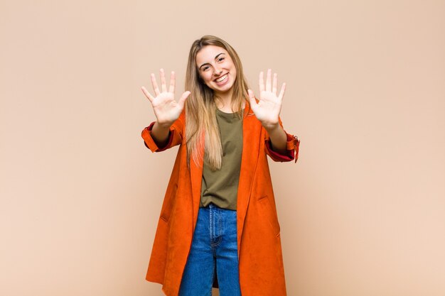 Mujer rubia sonriendo y mirando amistosamente, mostrando el número diez o décimo con la mano hacia adelante, contando hacia atrás