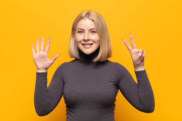 Mujer rubia sonriendo y mirando amistosamente, mostrando el número siete o séptimo con la mano hacia adelante, contando hacia atrás