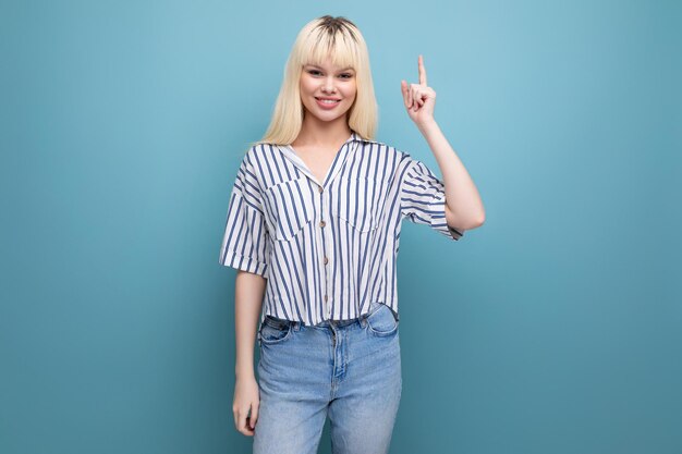 Una mujer rubia sonriente de un año con una blusa a rayas y jeans señala con el dedo hacia un lado