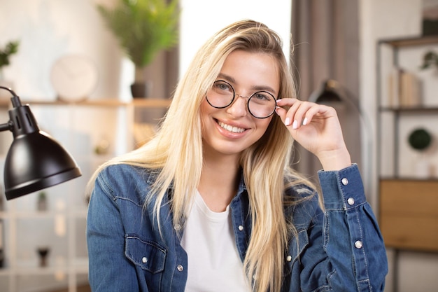 Mujer rubia sonriente con anteojos sentada en el escritorio en casa