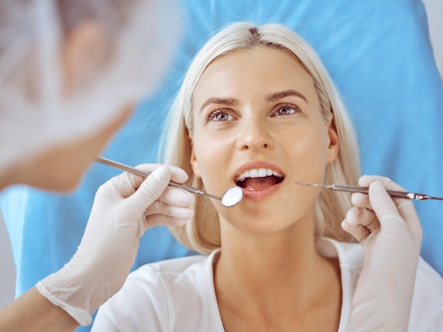Mujer rubia sonriente examinada por dentista en clínica dental. Dientes sanos y concepto de medicina.