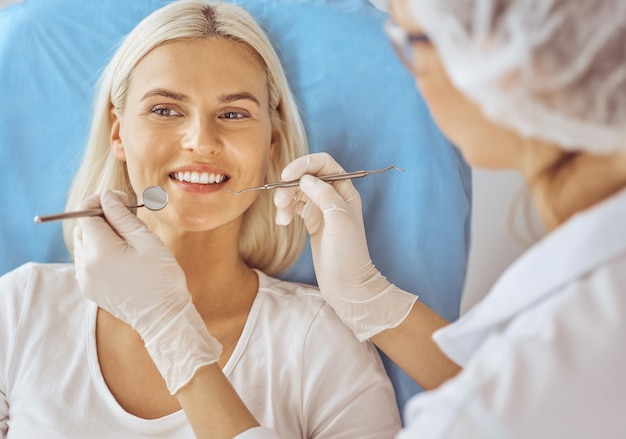 Mujer rubia sonriente examinada por dentista en clínica dental. Dientes sanos y concepto de medicina.