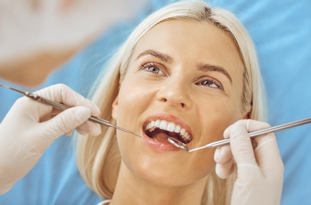 Mujer rubia sonriente examinada por dentista en clínica dental. Dientes sanos y concepto de medicina.