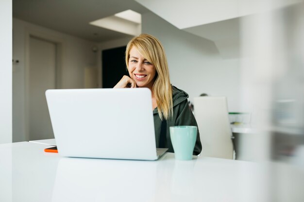 Mujer rubia sonriente de mediana edad con un portátil en un salón