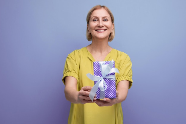 Mujer rubia sonriente sosteniendo una caja de regalo con un lazo para una sorpresa