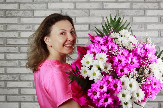 Mujer rubia sonriente sostiene un gran ramo de hortensias de crisantemo rosa y rosas envueltas en papel