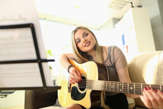 Mujer rubia sonriente tocando la guitarra y mirando notas
