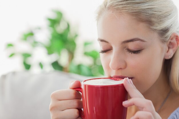 Mujer rubia sosteniendo una taza roja y bebiendo de ella