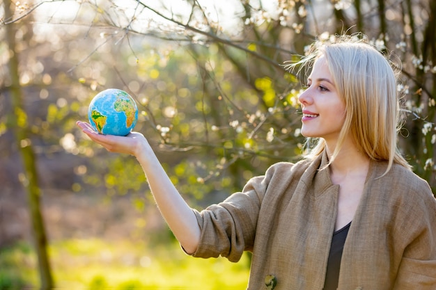 Mujer rubia sostiene globo terráqueo en jardín floreciente de cerezos