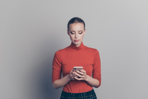 Mujer rubia con un suéter de cuello alto rojo posando contra la pared gris