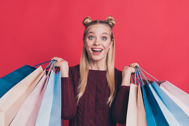 Mujer rubia con top-knots posando con bolsas de compras contra la pared roja