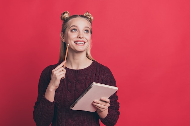 Mujer rubia con top-knots posando con un cuaderno contra la pared roja