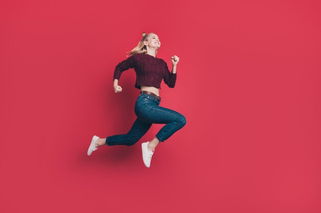 Mujer rubia con top-knots posando y saltando contra la pared roja