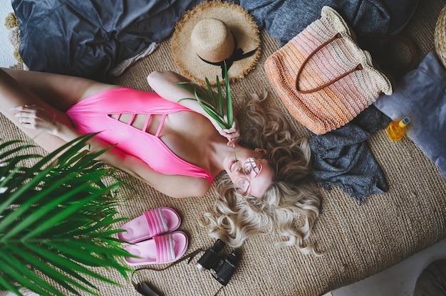 Mujer rubia en traje de baño rosa imitando el tiempo de vacaciones de verano playa en casa interior. Cuarentena divertida. Quedarse en casa, aislamiento.