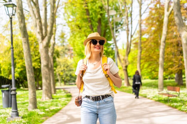 Una mujer rubia turista con sombrero y gafas de sol visitando en primavera un parque de la ciudad conociendo rincones del parque y tomando fotos con la cámara