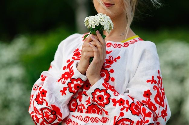 Foto mujer rubia ucraniana en camisa blanca y roja bordada cerrar retrato al aire libre sostener flores