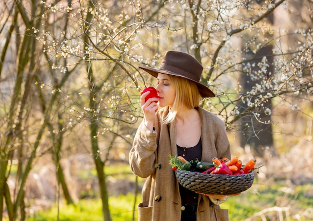 Mujer rubia con verduras en la cesta en jardín floreciente