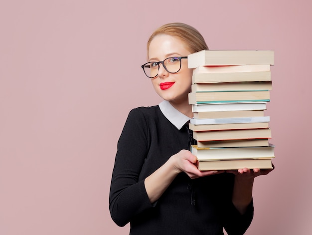 Mujer rubia vestida de negro con libros sobre rosa