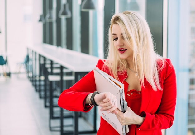 Una mujer rubia vestida de rojo mirando su reloj