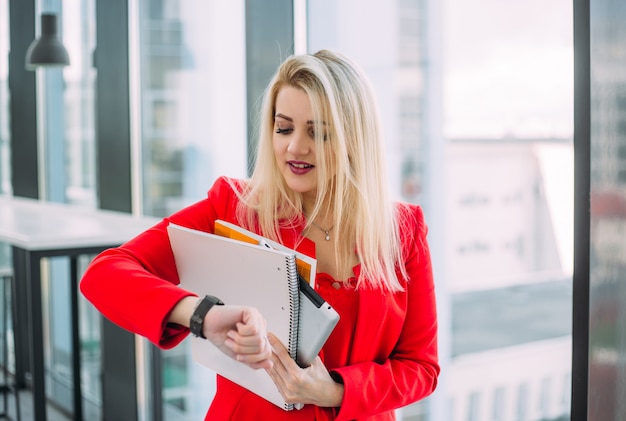 Una mujer rubia vestida de rojo mirando su reloj